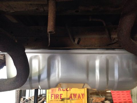1979 Ford Bronco - The underside of a vehicle showing a new, silver fuel tank installed between two sections of the exhaust system. A yellow sign with red let…