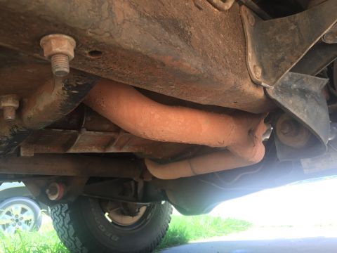 1993 Ford Bronco - The underside of a vehicle shows a rusty frame with exhaust pipes covered in dirt. A tire and part of the wheel well are visible in the low…