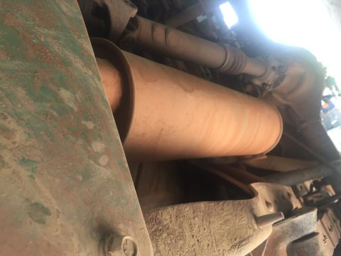 1993 Ford Bronco - The underside of a vehicle shows a large, cylindrical muffler with a tan, dusty surface. A rusty green metal panel is visible on the left,…