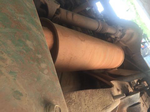 1993 Ford Bronco - Underside view of a vehicle's exhaust system, featuring a large, cylindrical muffler that appears to be orange or tan in color. A green, ru…