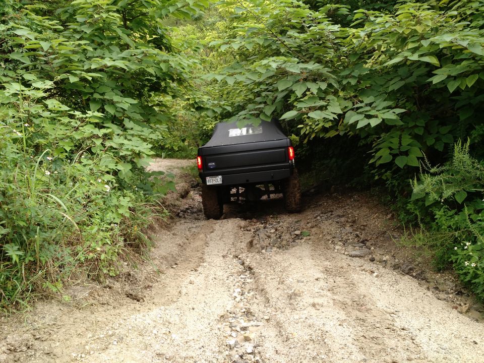 Black 1992 Ford Bronco driving up a muddy, wooded trail.
