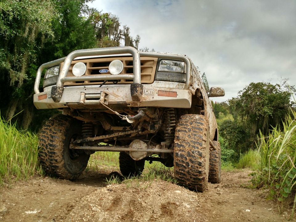 Muddy 1992 Ford Bronco with bull bar and off-road tires on a dirt trail.