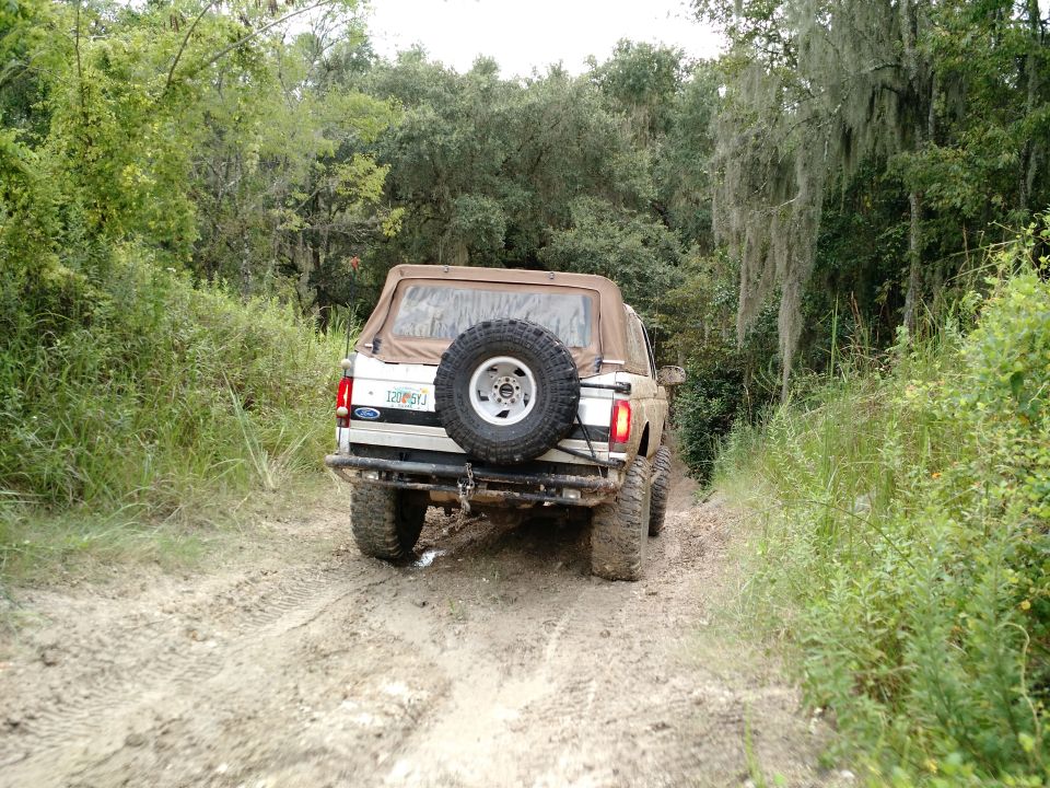 1992 Ford Bronco driving on a muddy road.