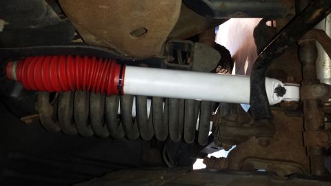 1996 Ford Bronco - Underbody close-up of a newly installed white-bodied shock absorber with a red rubber boot, mounted in front of a black coil spring on a fr…