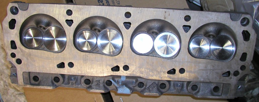 Bare cast-iron cylinder head with four combustion chambers and freshly machined valves on cardboard