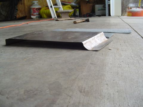 1999 Ford Taurus - A flat bent sheet-metal panel with a rolled, ground-bright edge lying on a concrete garage floor, shot from ground level. A rolled strip of…