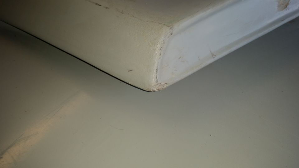 Close-up of a chipped corner on a light-colored vehicle body panel.
