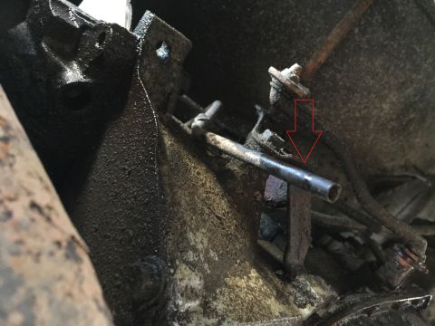 1989 Ford Bronco - A close-up, low-angle view of a greasy, dark-colored vehicle transmission housing and related components. A red arrow points to a metal tub…