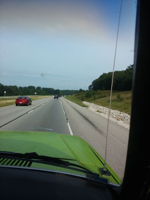 1986 Ford Bronco - View from the interior of a bright green vehicle driving on a highway. A red sedan is visible in the left lane ahead.
