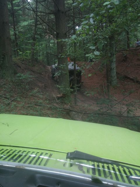 1986 Ford Bronco - A green vehicle's hood and windshield wipers are in the foreground, looking out at a wooded trail where two off-road vehicles are navigatin…