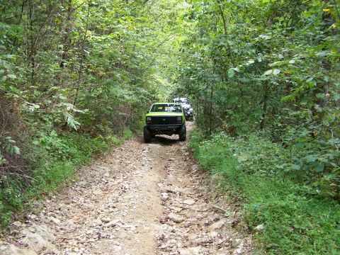 1986 Ford Bronco - A lime green Ford Bronco is driving down a narrow, rocky dirt road surrounded by dense green foliage. Another vehicle is visible further do…