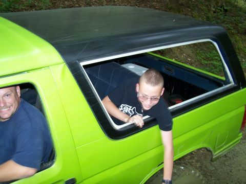 1986 Ford Bronco - Two men are in a bright green Ford Bronco with a black soft top, with one man leaning out the passenger window. The vehicle appears to be i…