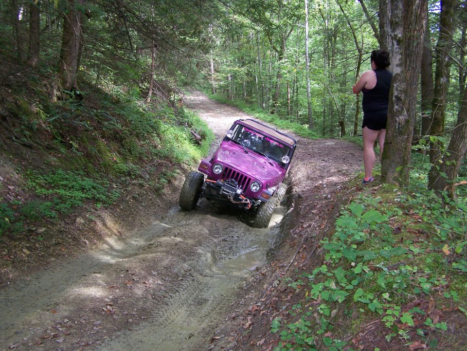 Purple Jeep Wrangler driving through a muddy forest trail.