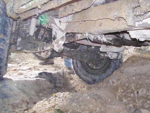 1986 Ford Bronco - The underside of a heavily mud-covered vehicle, likely an off-road SUV or truck, is shown with its suspension and drivetrain components vis…