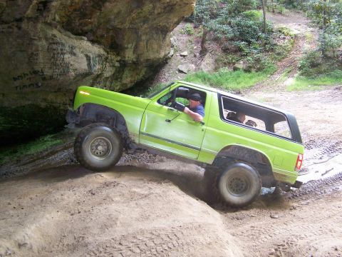 1986 Ford Bronco - A bright green 1980s Ford Bronco is driving off-road through a muddy cave entrance. The vehicle has large off-road tires and the driver is…