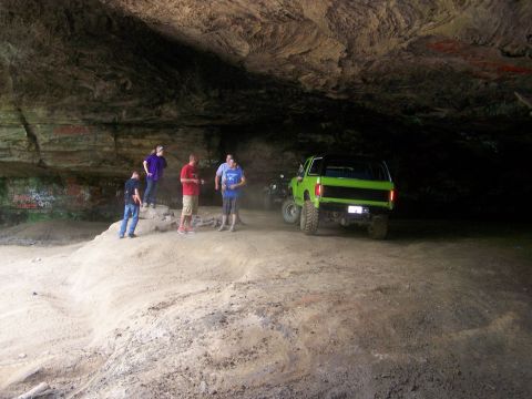 1986 Ford Bronco - A bright green 1986 Ford Bronco is parked inside a cave with a group of people standing around it.