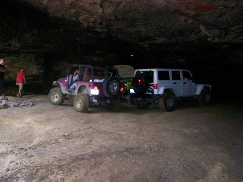 1986 Ford Bronco - Two modified Jeep Wranglers are parked inside a dark cave with rough, sandy ground. One is purple and modified for off-roading, while the o…