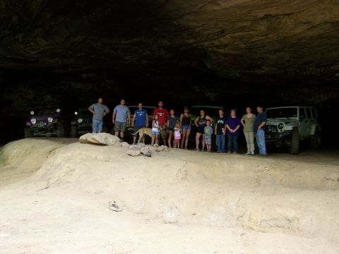 1986 Ford Bronco - A group of people and two dogs stand in front of several off-road vehicles inside a large cave.