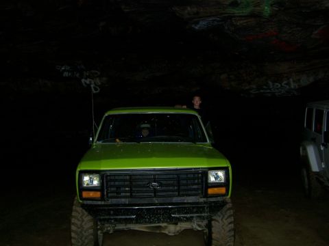 1986 Ford Bronco - A bright green lifted Ford Bronco is parked inside a dark cave with graffiti on the walls. Another vehicle, possibly a Jeep, is parked to t…