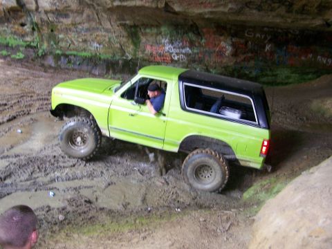 1986 Ford Bronco - A bright green 1986 Ford Bronco is driven through a muddy cave with graffiti on the walls. The driver is visible behind the wheel, and the…
