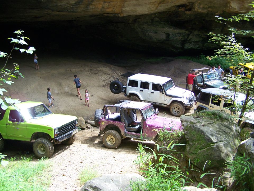Lime green 1986 Ford Bronco parked in front of a cave with people and other off-road vehicles.