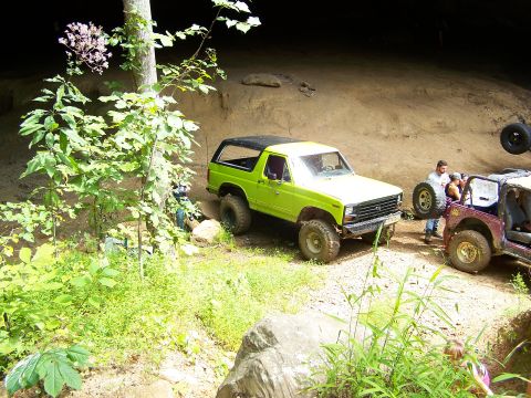 1986 Ford Bronco - A bright green Ford Bronco is parked on a dirt path next to a purple Jeep. Both vehicles appear to be off-roading in a wooded area with ste…