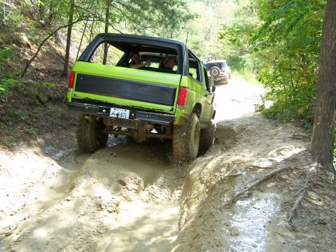 1986 Ford Bronco - A bright green 1986 Ford Bronco is driving through a muddy trail with another white SUV behind it. The Bronco is tilted to the side as it n…