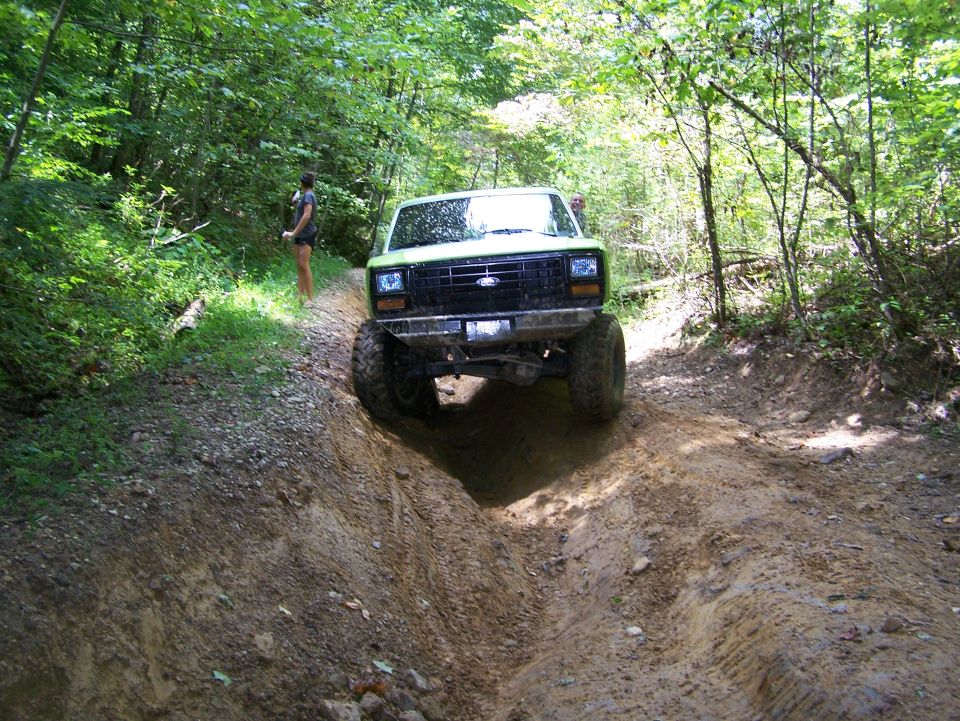 Green lifted Ford Bronco driving down a muddy trail in the woods.