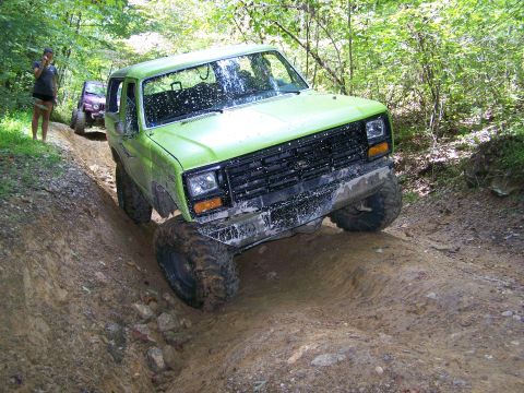 1986 Ford Bronco - A bright green Ford Bronco is navigating a steep, muddy trail with large off-road tires. Another purple SUV is visible further up the trail…