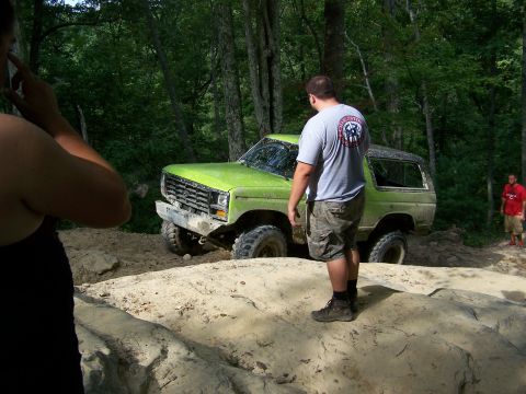 1986 Ford Bronco - A bright green Ford Bronco is positioned on a rocky trail with a man standing behind it, looking away from the camera. Another man in a red…