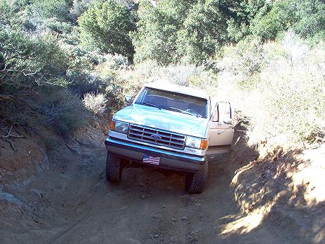1988 Ford Bronco - Ford Bronco tackles a challenging off-road trail with steep inclines and dense vegetation.