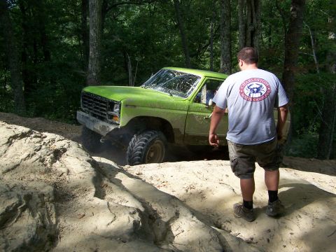 1986 Ford Bronco - A man stands on a dirt trail looking at a bright green 1980s Ford Bronco as it navigates the rough terrain. The Bronco is angled towards th…