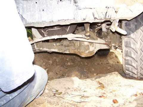 1986 Ford Bronco - The underside of a vehicle, likely an SUV, is shown with its suspension and drivetrain components covered in mud. A tire and part of the ve…