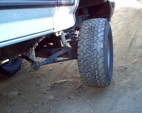 1988 Ford Bronco - Detail shot of the suspension and tire of a vehicle on a dusty, uneven surface.