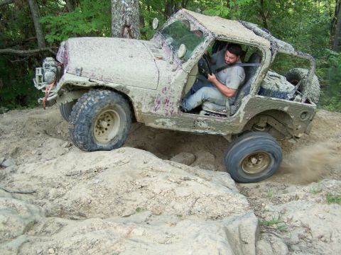 1986 Ford Bronco - A mud-covered Jeep Wrangler is navigating a rocky, off-road trail with a driver behind the wheel. The vehicle is tilted at an angle as it c…