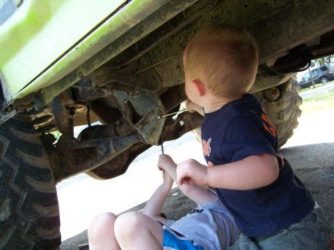 1986 Ford Bronco - Two young children are working on the undercarriage of a lifted, lime green vehicle, possibly a Ford Bronco, with large tires. One child is…