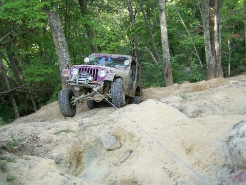 1986 Ford Bronco - A purple, mud-covered Jeep Wrangler is being pulled up a steep, sandy incline by a winch cable. The vehicle is positioned at an angle on th…