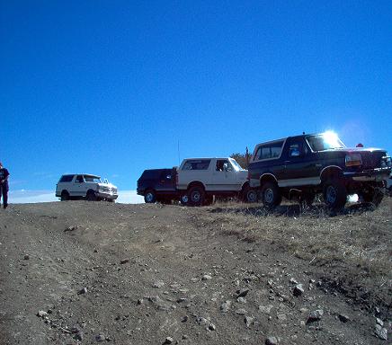 1988 Ford Bronco - Four SUVs are parked on a dirt hill under a clear blue sky.