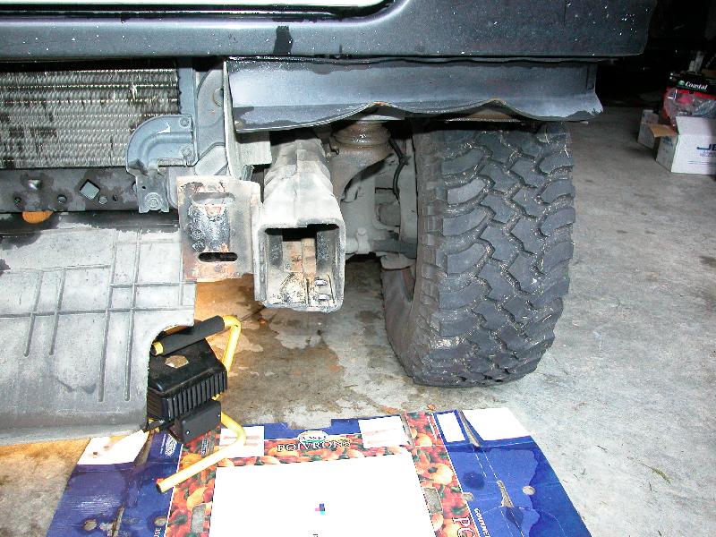 Exposed front frame rail and bumper bracket on a truck with the bumper removed, mud-terrain tire beside it