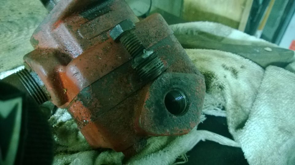 Red metal part with bolt and threaded openings, resting on cloth
