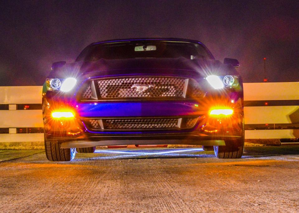 Front view of a purple Ford Mustang with its headlights and fog lights on at night. The grille has a horse emblem