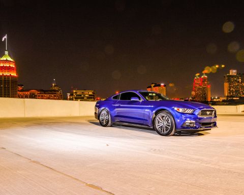 2015 Ford Mustang - A blue 2015 Ford Mustang is parked on a rooftop overlooking a city skyline at night.