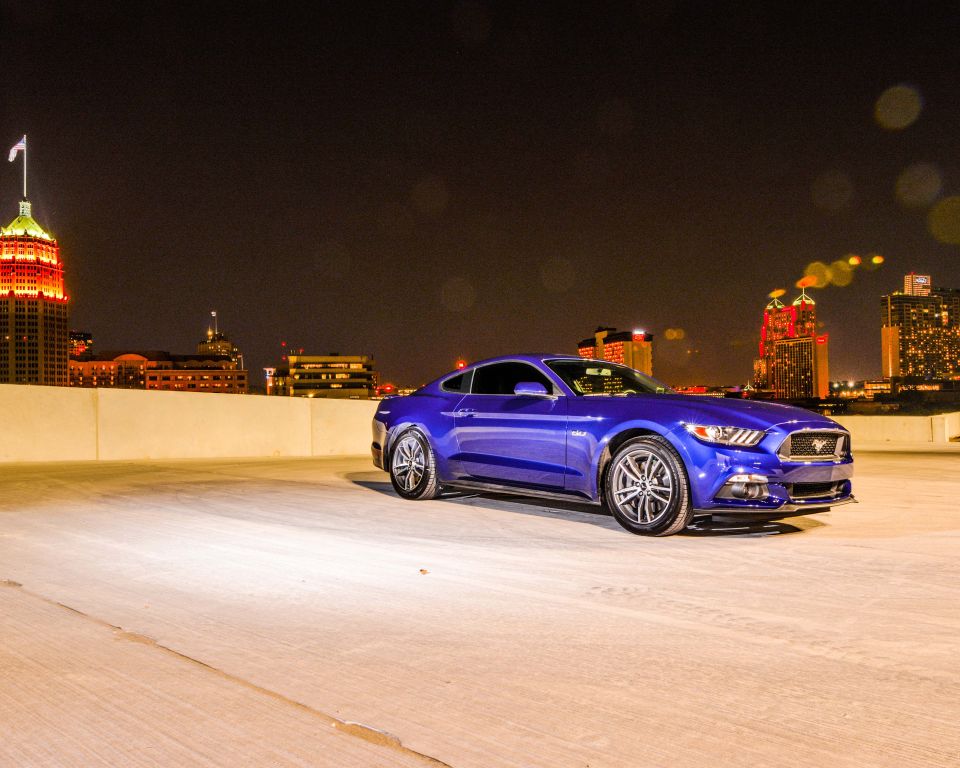 Blue 2015 Ford Mustang parked on a rooftop at night with city lights in the background