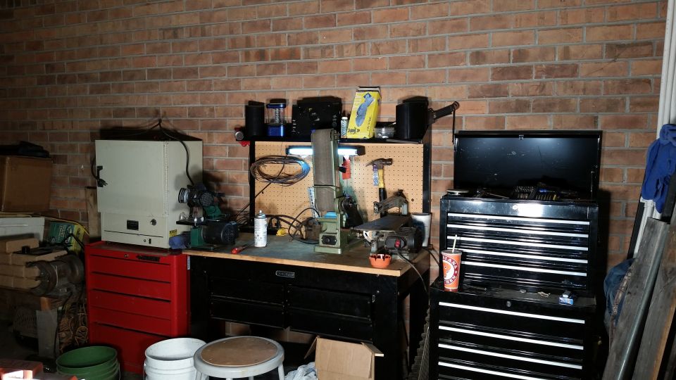 Workbench with belt sander, drill press, and tool chests against a brick wall