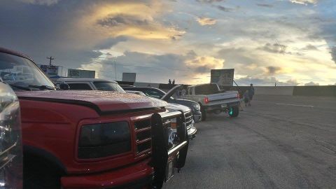 1995 Ford Bronco - Several trucks and cars are parked in a lot during sunset with dramatic clouds overhead.