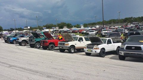 1995 Ford Bronco - A white Ford Bronco is parked with its hood up among many other trucks at an outdoor event.
