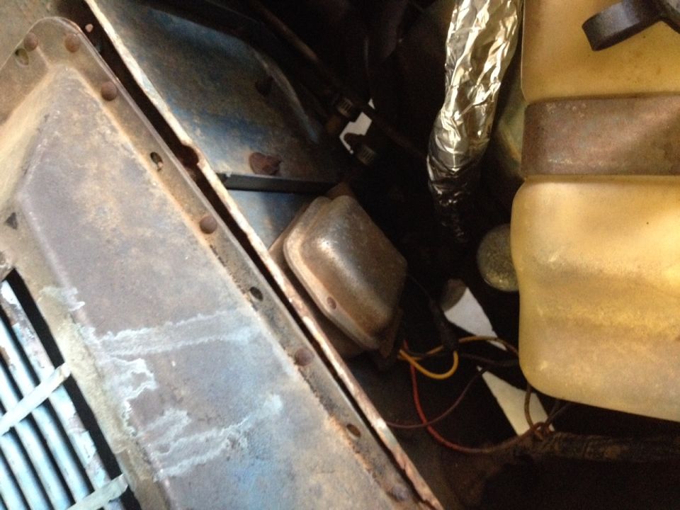 Close-up of a vehicle's voltage regulator with wires and part of a coolant reservoir