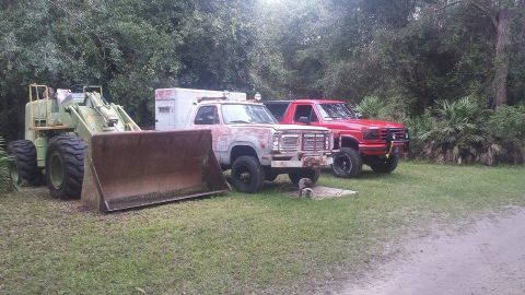 1995 Ford Bronco - A front loader, a Dodge Ramcharger, and a Ford F-150 are parked outdoors in a grassy area.