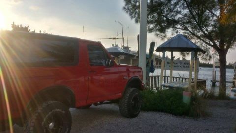 1995 Ford Bronco - Red 1995 Ford Bronco parked near a waterfront, with a bridge visible in the distance.
