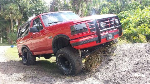 1995 Ford Bronco - This red Ford Bronco is shown navigating an off-road course, a prominent aftermarket grille guard.